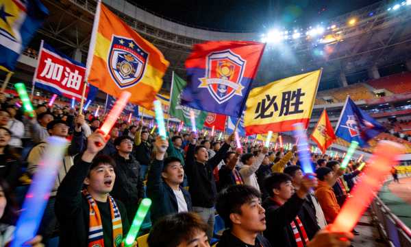 体育场馆内观众席上球迷高举助威旗帜，现场气氛热烈